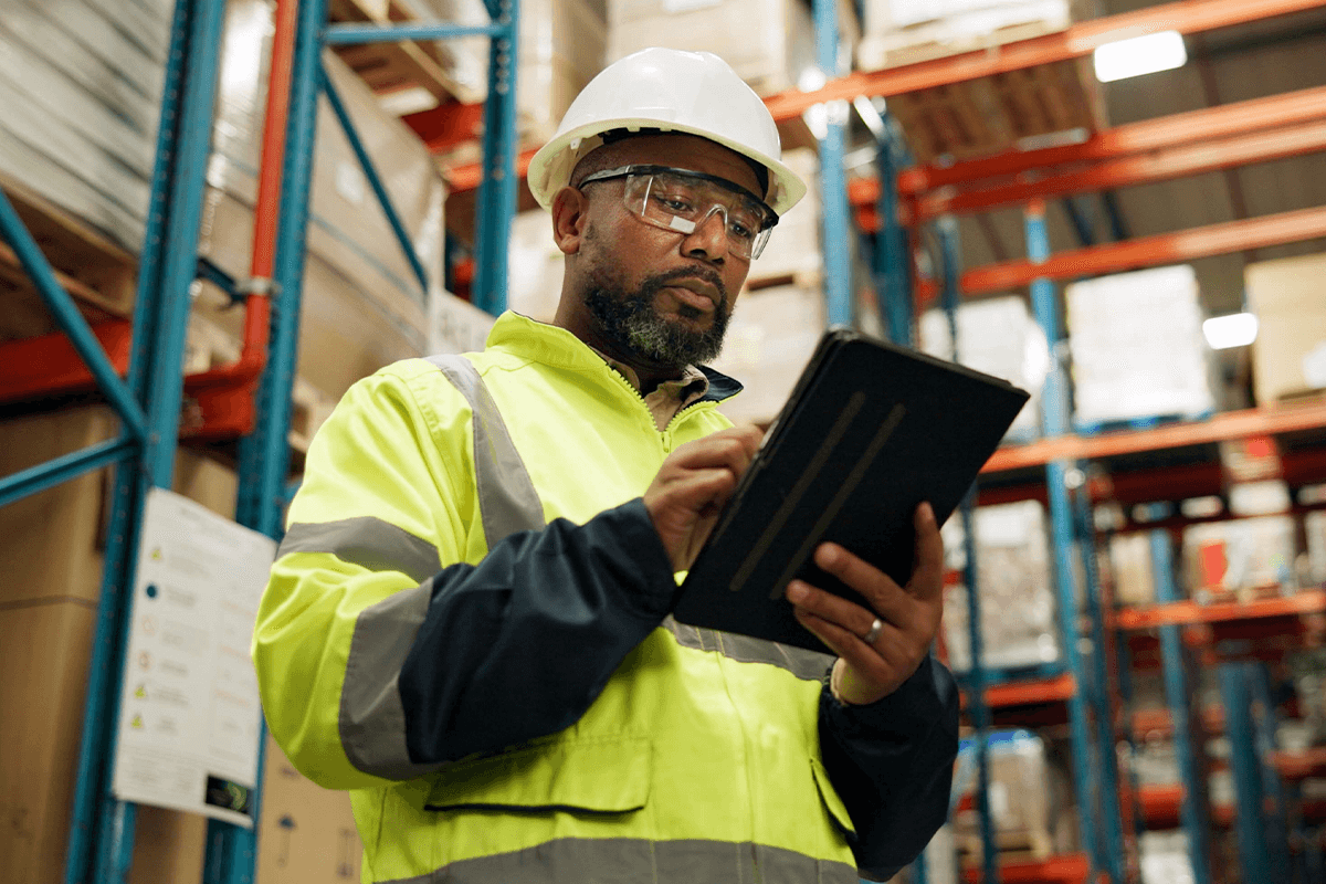 Warehouse worker wearing helmet viewing tablet
